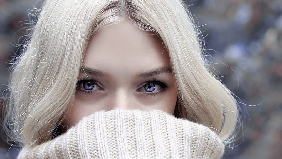 Müde Augen: Blone Frau mit blauen Augen, die Pulli über Nase gezogen hat