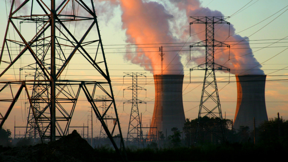 Atomkraft: Atomkraftwerke bei Sonnenuntergang, davor Strommasten.