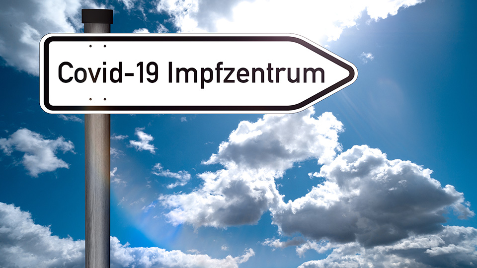 Schild mit der Aufschrift: Covid-19 Impfzentrum vor blauem Himmel mit Wolken
