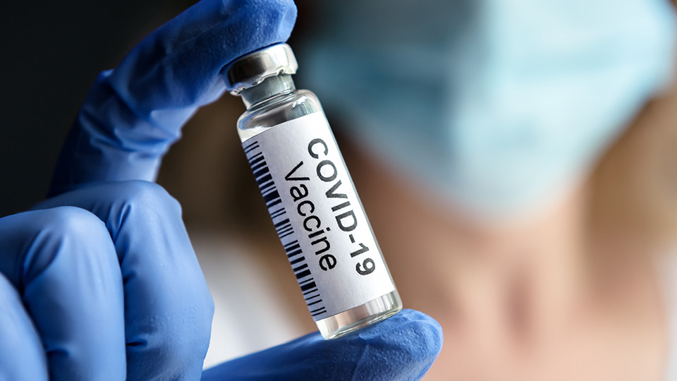 Corona-Impfstoff in einer Hand mit blauem Einweg-Handschuh