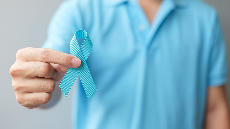 Männliche Person mit einem hellblauen Oberteil, der eine hellblaue Schleife hält und zeigt.