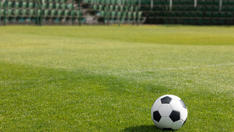 Fußball auf grünem Rasen vor leeren Sitzreihen im Stadion.