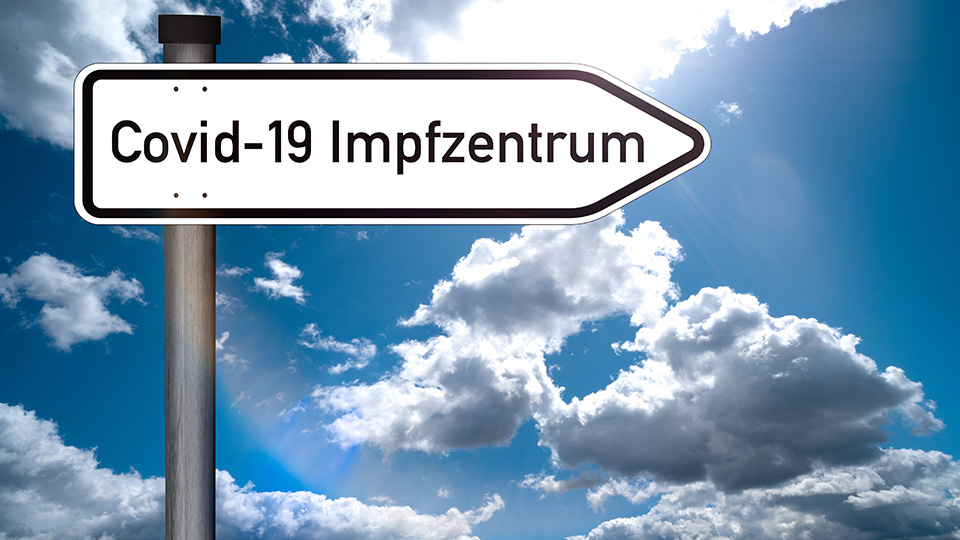 Schild mit der Aufschrift: Covid-19 Impfzentrum vor blauem Himmel mit Wolken