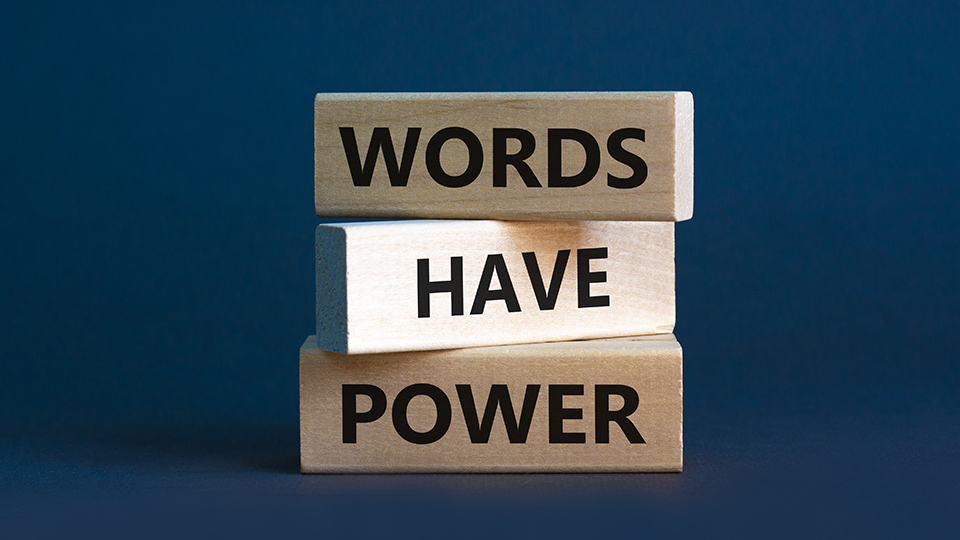 Auf blauem Hintergrund stehen auf drei übereinander gestapelten Holzklötzen die Worte "Words Have Power"