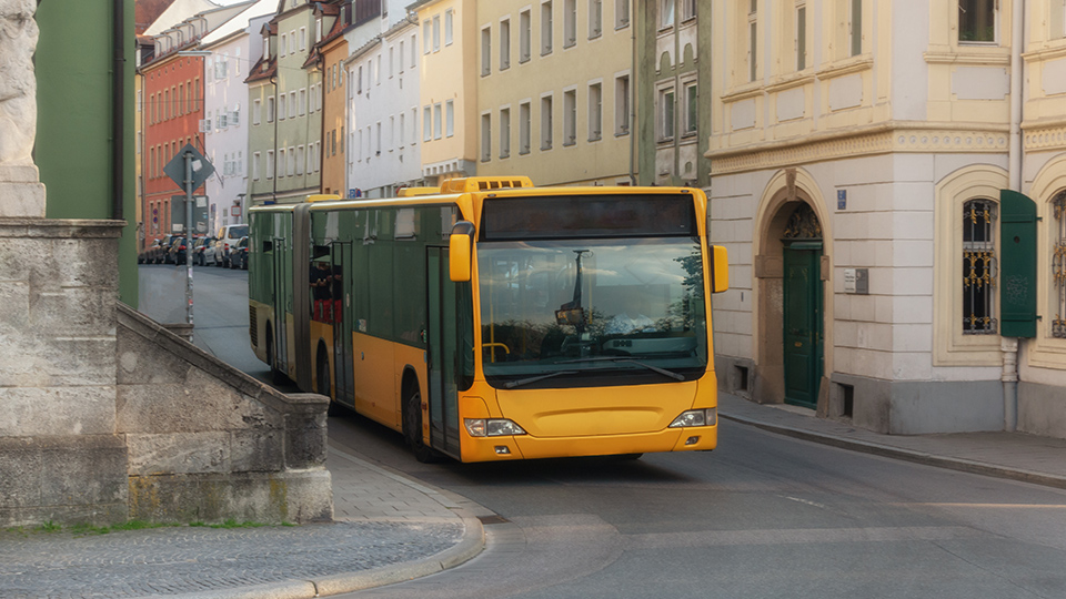 Gelber Stadtbus, der gerade durch die Gasse von Regensburg fährt.