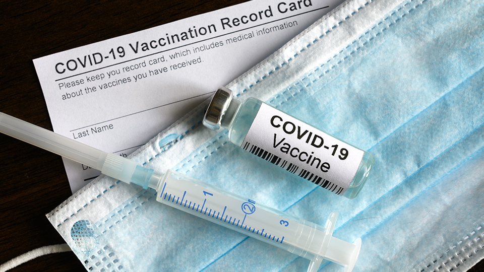 Covid-19 Impfungstoff liegt neben einer Spritze auf einer OP-Maske.