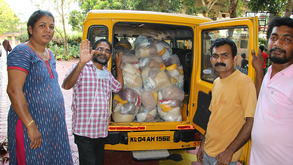 Drei Männer und eine Frau aus Indien, die vor einem gelben Lieferwagen stehen, der hinten die Türen geöffnet hat, wo Säcke mit Spenden hervorschauen.