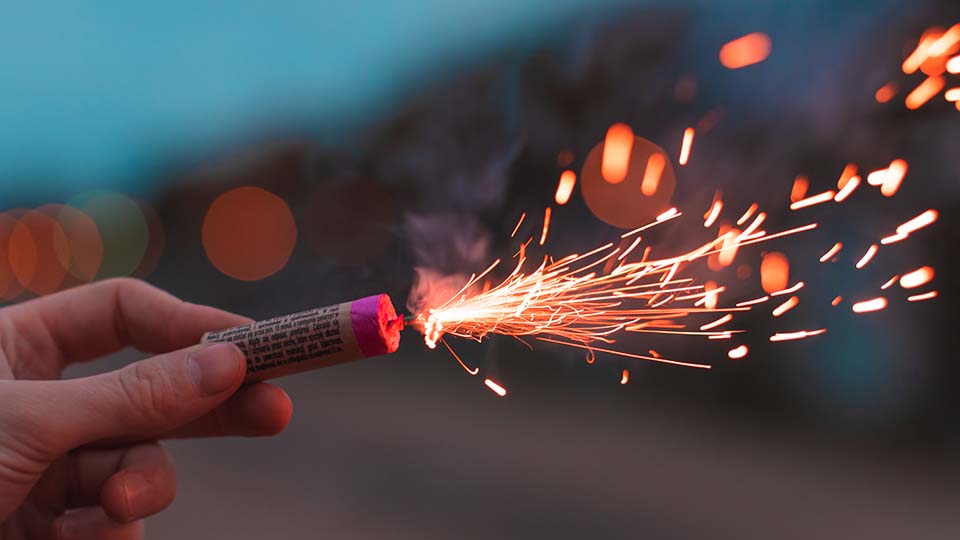 Hand, die einen bereits entzündeten Feuerwerkskörper hält.