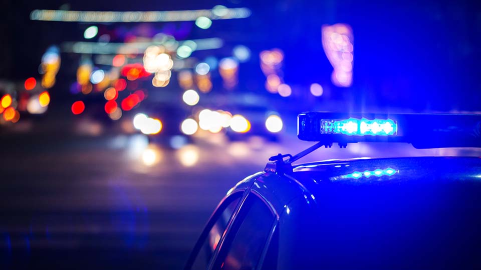 Polizei Auto bei Nacht von hinten mit Blaulicht. Im Hintergrund verschwommene Lichter.