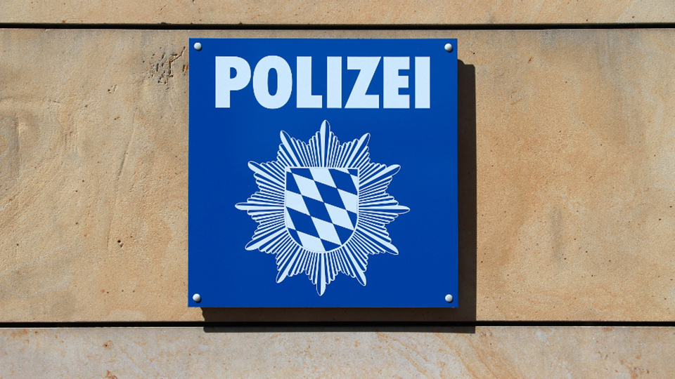 Polizei Schild in Blau-Weiß, das an einer beigen Wand hängt.