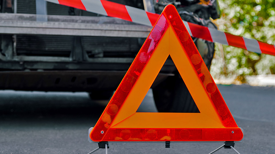 Warndreieck im Vordergrund und beschädigtes Auto im Hintergrund.