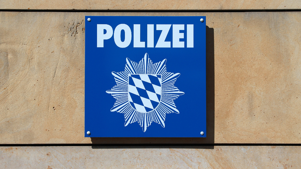 Polizei Schild in Blau-Weiß, das an einer beigen Wand hängt.