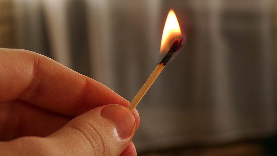 Hand, die ein entzündetes Streichholz hält.