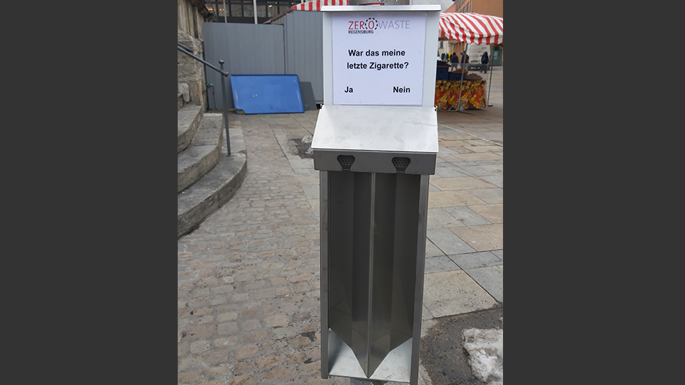 Neuer Sammelbehälter für Zigaretten in der Regensburger Innenstadt. Auf diesem steht die Aufschrift: "War das meine letzte Zigarette?" 