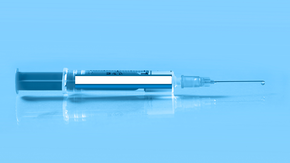 Dunkelblaue liegende Spritze mit Impfstoff vor hellblauem Hintergrund.