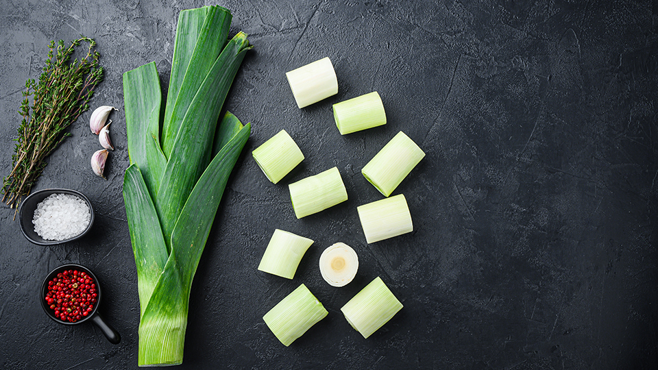 Lauch, bei dem der untere weiße Teil in kleine Stücke geschnitten daneben liegen. Links vom großen Lauchstängel steht Salz und Chilli sowie frischer Rosmarin. 