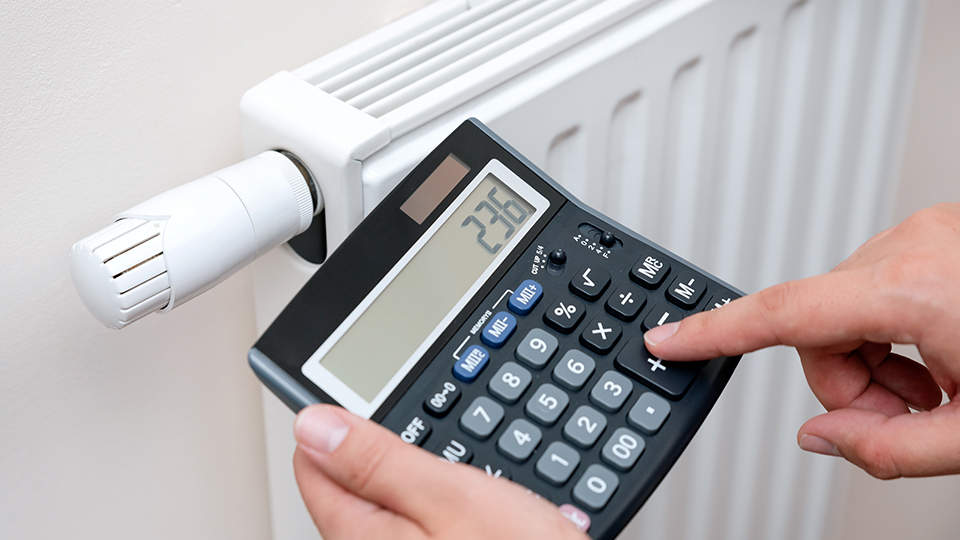 Eine Heizung und davor eine Hand, die einen Betrag in einen Taschenrechner eingibt.