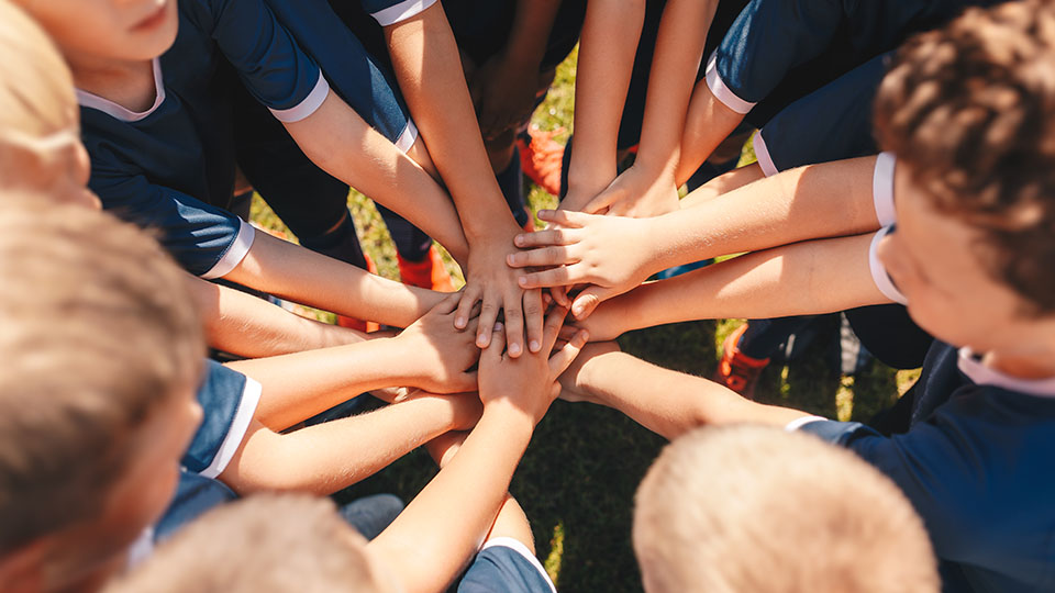Mehrere Jungen, die Mitglieder eines Sportteams sind, stehen im Kreis und legen ihre Hände als Einstimmung auf ein Spiel übereinander.
