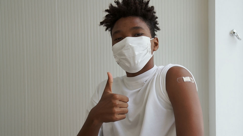 Teenager mit Maske zeigt das Daumen-Hoch-Zeichen nach seiner Impfung.