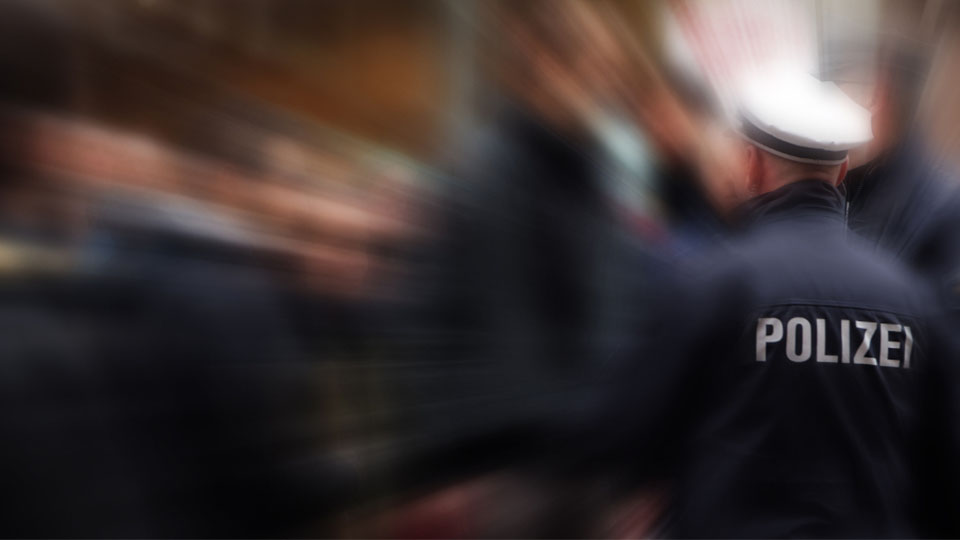 Mehere Polizeibeamte von hinten. Einer davon scharf dargestellt, wobei der Schriftzug "POLIZEI" auf seiner Jacke im Fokus steht.