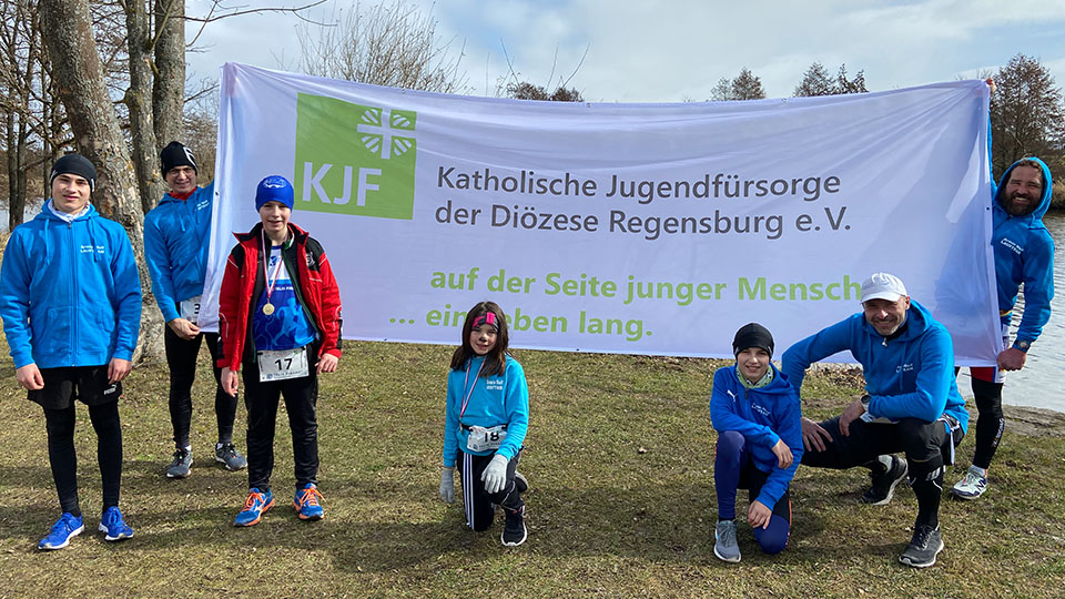 Teilnehmer des Benefizlaufs "Wir bauen Brücken" mit einem großen Schild der Katholischen Jugendfürsorge der Diözese Regensburg.