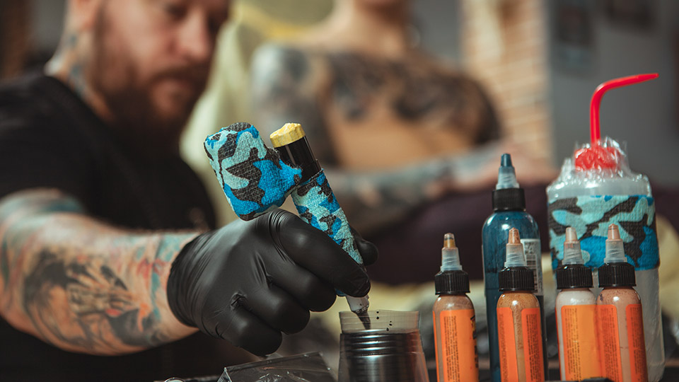 Tätowierter Mann, der gerade Tattoofarben anmischt.