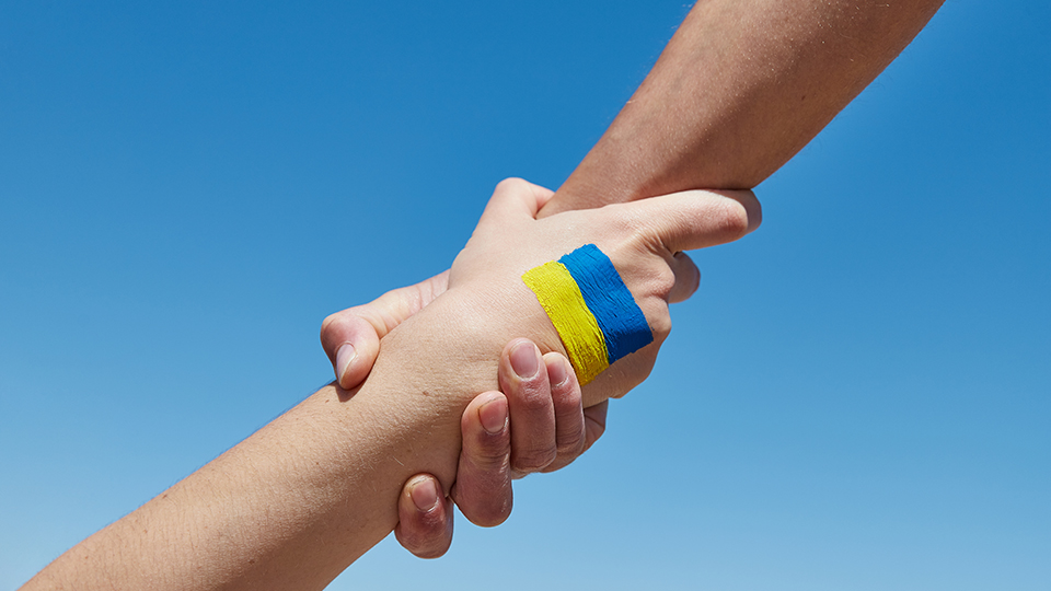 Eine Hand von oben nimmt eine andere Hand, auf der eine ukrainische Flagge ist.