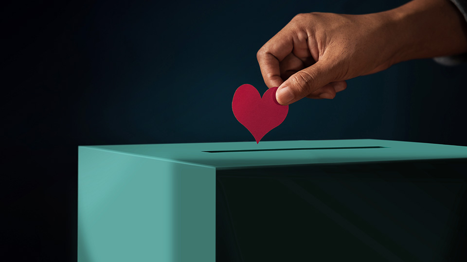 Eine männliche Hand wirft gerade ein rotes Papierherz in eine Spendenbox.