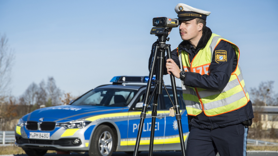 Polizeibeamter mit Radarfalle vor Einsatzfahrzeug