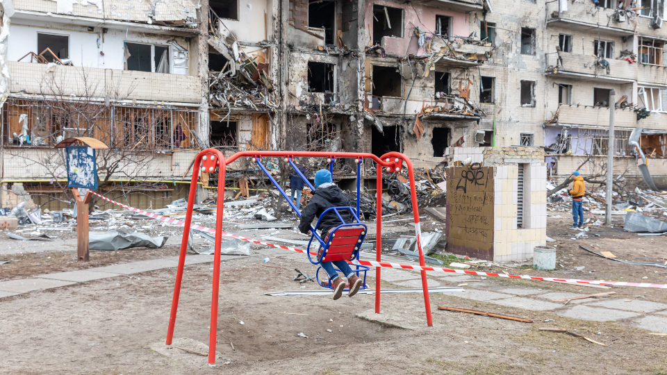 Ukrainischer Junge schaukelt vor zerbombtem Häuserblock