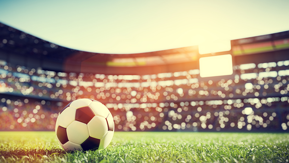 Fußballstadtion mit einem Fußball im Vordergrund, der auf dem Spielfeld liegt.
