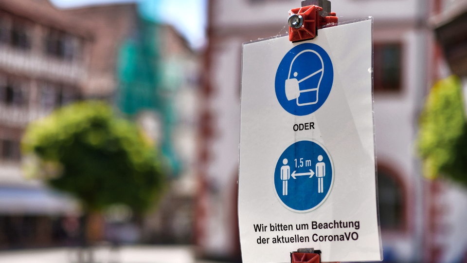 Ein Schild mit Corona Regeln in einer Altstadt