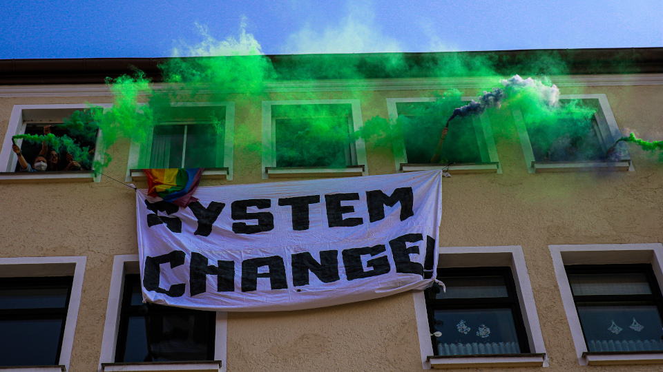 Plakat mit der Aufschrift System Change vor einem Haus