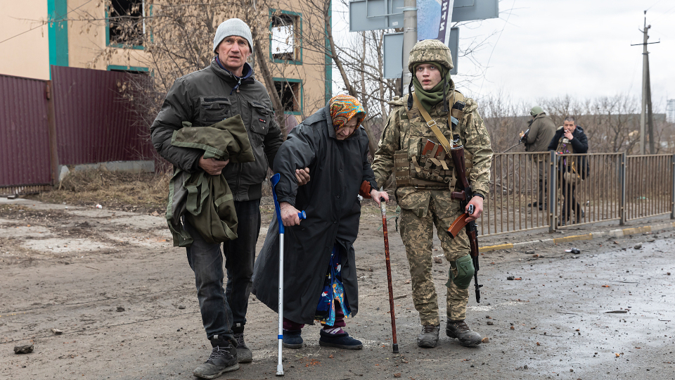 Eine ältere Geflüchtete wird von einem Soldaten und einem Mann gestützt
