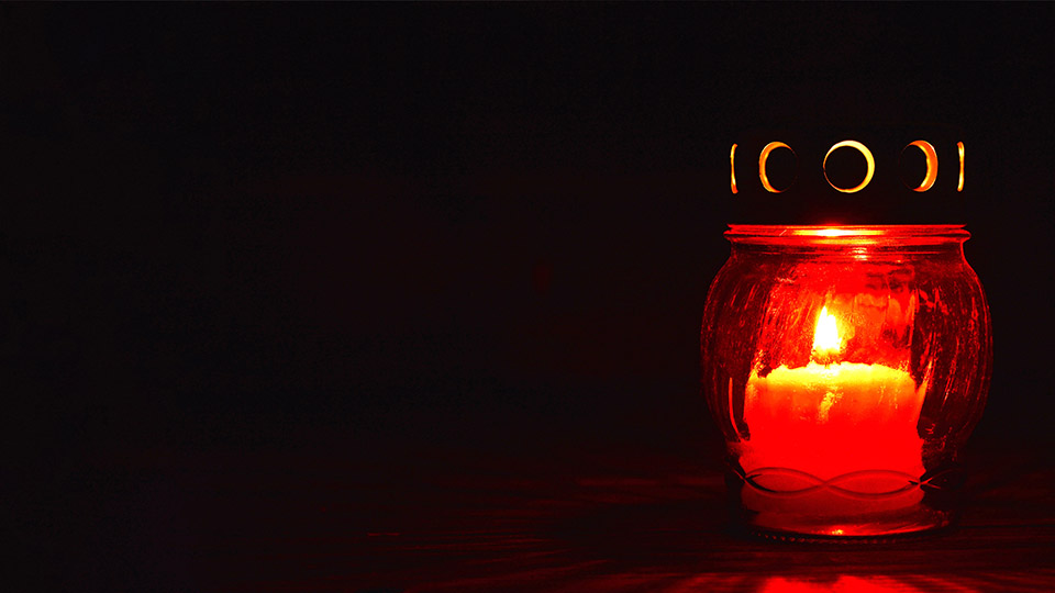 Brennende rote Grabkerze vor schwarzem Hintergrund