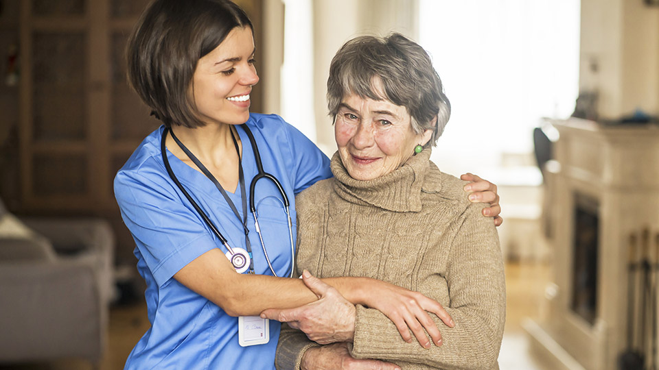 Pflege mehr wertschätzen: Pflegerin, die eine ältere Dame umarmt und anlächelt.