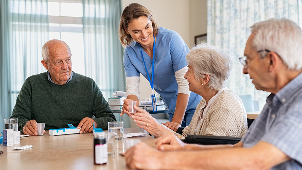 35-Stunden-Woche in der Pflege: Altenpflegerin, die lächelnd mit Bewohnern eines Pflegeheims spricht.
