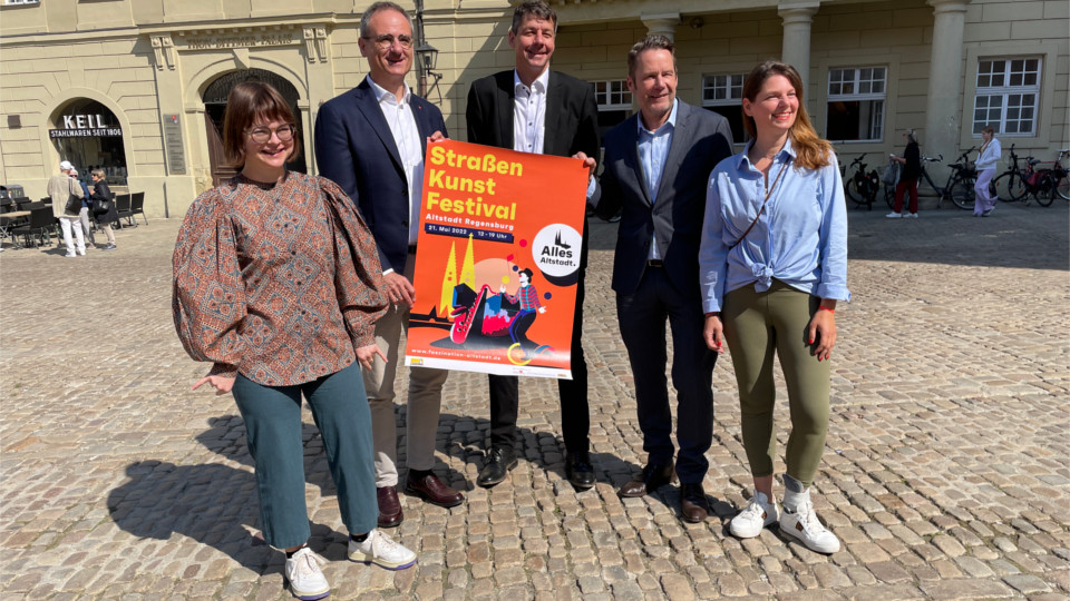 Die Verantwortlichen für das Straßenkunstfestival präsentieren am Haidplatz in Regensburg das Werbeplakat