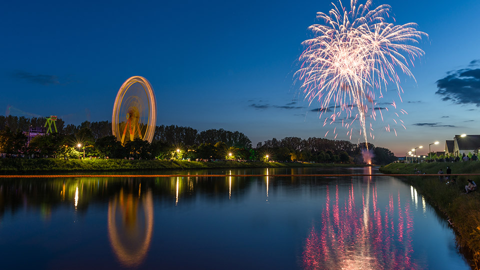 Kulisse der Regensburger Maidult am Abend von der Donau aus: Feuerwerk und Riesenrad im Fokus.