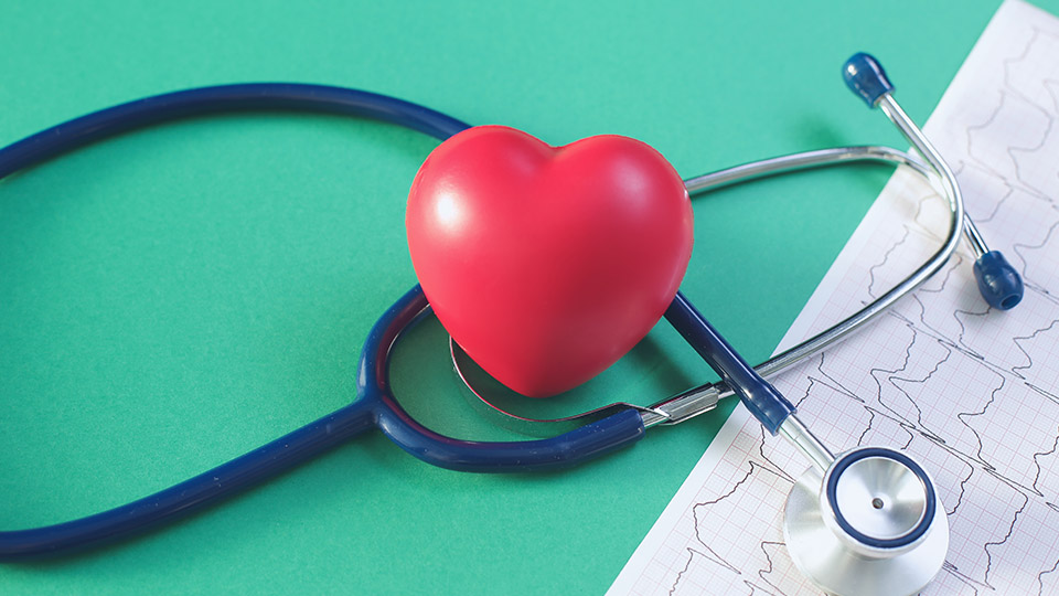 Blaues Stethoskop und darauf liegend ein rotes Herz auf grünem Hintergrund. 