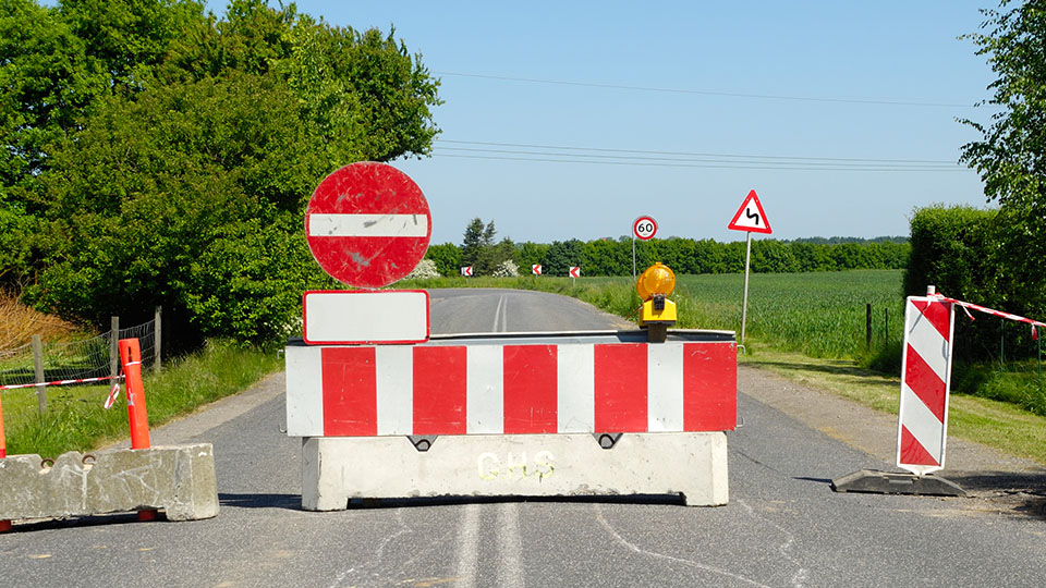 Straßenbauarbeiten, Schild, das eine Straßensperrung anzeigt und eine Schranke, die eine Durchfahrt verhindert.
