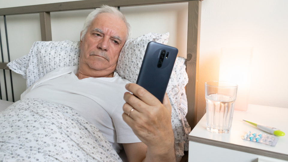 aging senior man male in bed at home flat tired sick ill alone retired resting virus taking care, holding talk smartphone