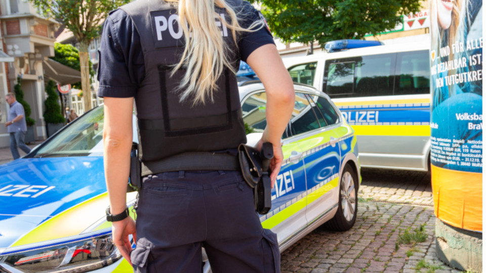 Großeinsatz der Polizei: Blonde Polizistin von hinten mit Hand an der Dienstwaffe.