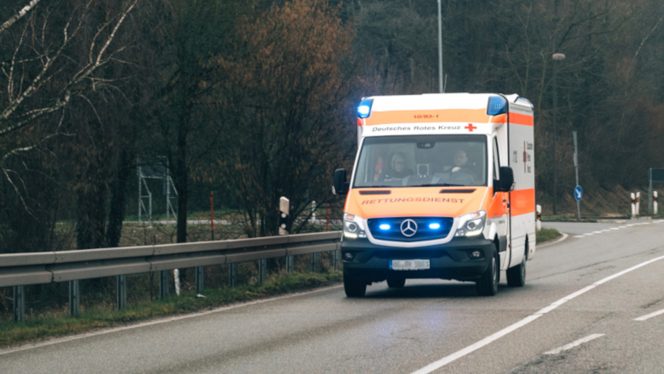 Motorrad mit Krankenwagen kollidiert: Krankenwagen, der gerade mit Blaulicht eine Straße entlangfährt.
