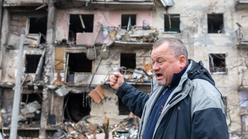 Ukrainischer Mann vor zerbombter Hausversade