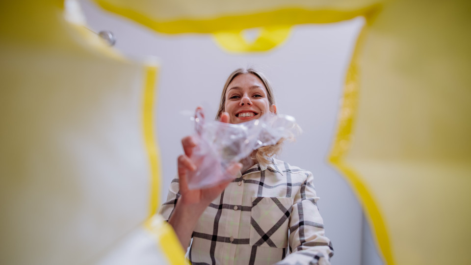 Eine Frau, die ihren Plastikmüll in einen Gelben Sack wirft und lächelt.