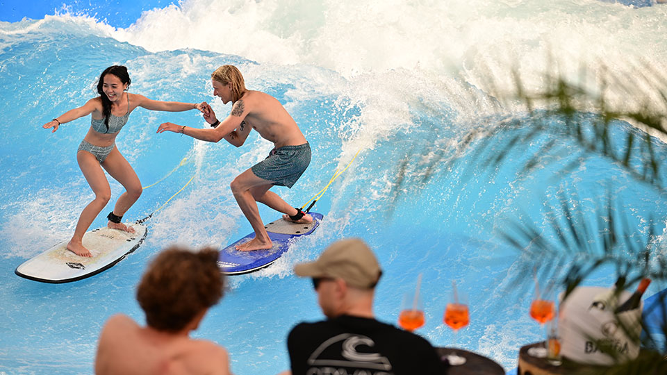 Terrassen-Opening der Citywave am DEZ: Surfer, die gerade auf der Welle surfen, im Vordergrund Drinks.