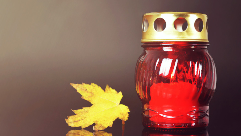 Rote Grabkerze auf dem Boden und dahinter Laubblätter am Boden.