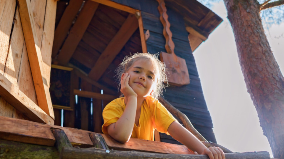 Mädchen, die von dem Baumhaus auf einem Spielplatz herunterblickt.