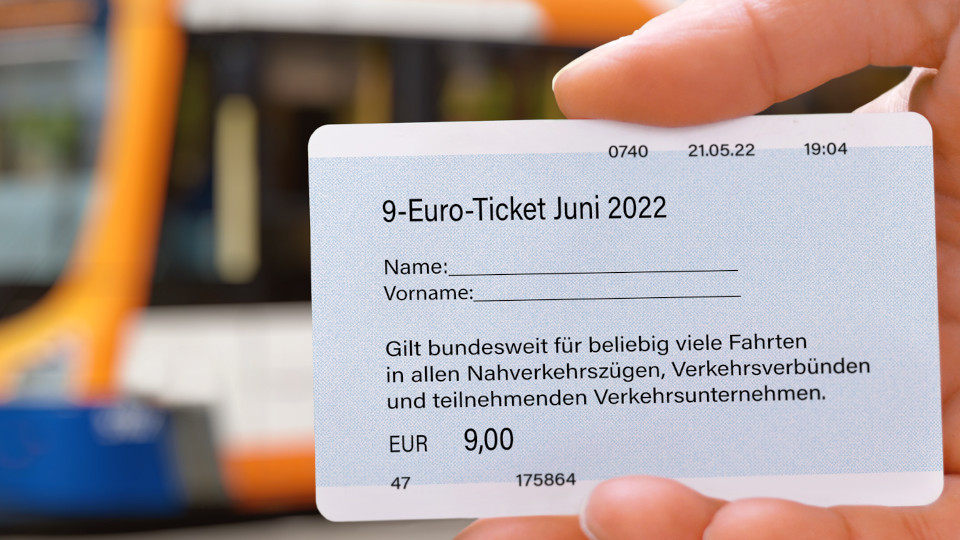 9-Euro-Ticket in der Hand und im Hintergrund ein Bus.